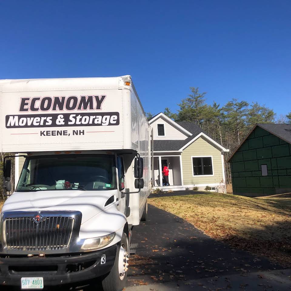 Economy Movers truck sitting in driveway of a tan  colored house with a blue sky in the background