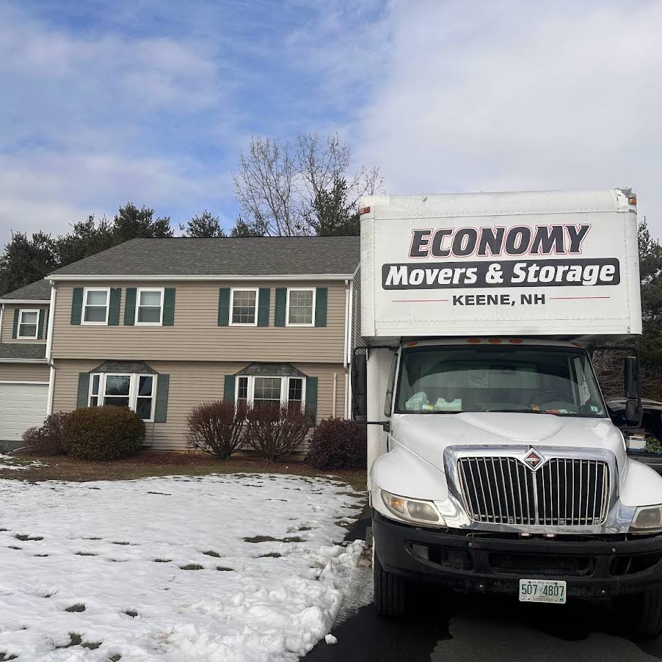 Economy Movers truck in driveway of two level tan house with snow on the ground