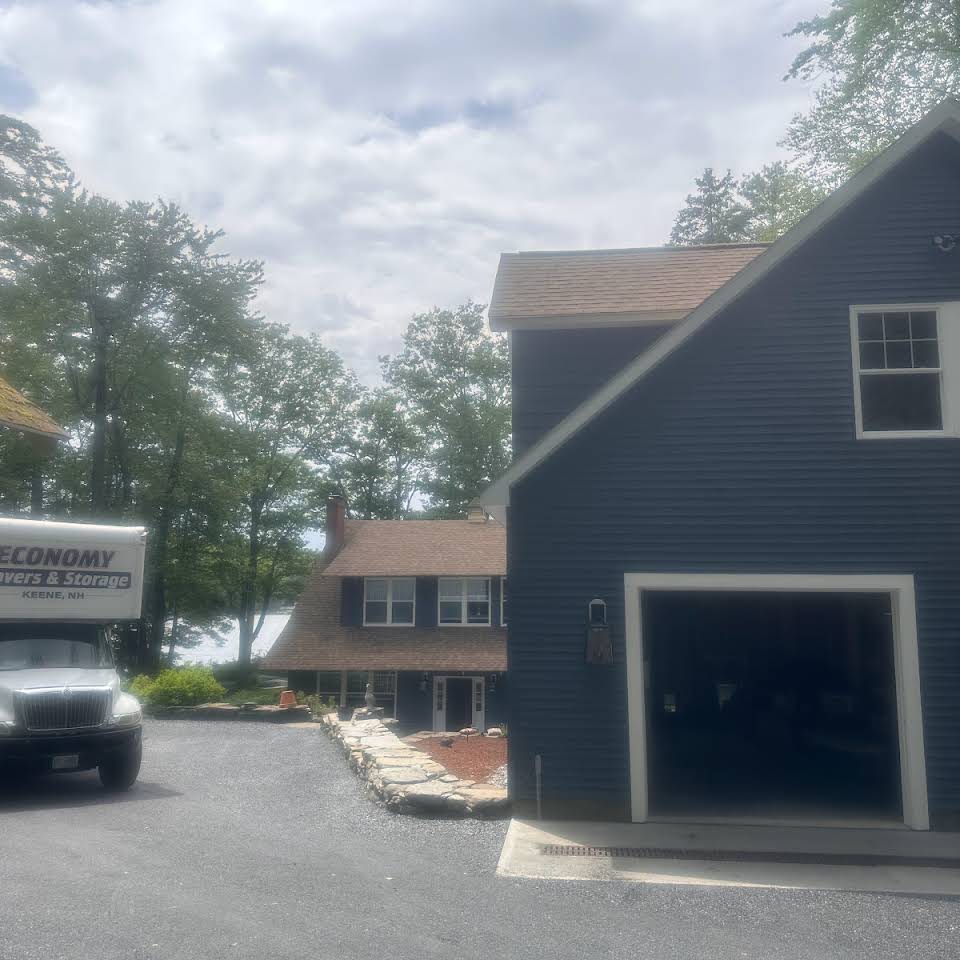 Economy Movers truck sitting outside of a blue house's garage and in front of another brown house